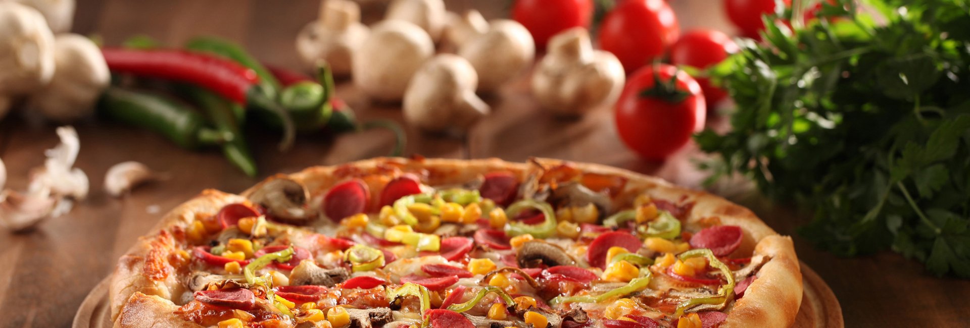 Pizza topped with pepperoni, peppers, mushrooms and corn on a wooden board